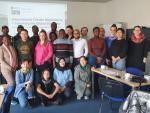 A group of people from different backgrounds stand together smiling for a group photo in a seminar room. 