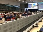A conference room filled with delegates attending the EU-LAC Policy Dialogue on Nature-Based Solutions. The attendees are seated at desks arranged in a U-shape, engaging in discussions and using laptops. A large screen at the front displays the event title 'EU-LAC Policy Dialogue on Nature-Based Solutions' with the date '26-27 June 2024, Brussels, Belgium'.