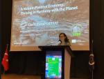 Dr. Daniela Rizzi stands at a podium giving a presentation titled “A Nature-Positive Economy: Thriving in Harmony with the Planet” at the SURE Conference 2025 in Istanbul. The large screen behind her displays the GoNaturePositive! logo and European Union funding acknowledgment, with a river landscape as the background. Turkish and conference flags flank the stage.