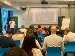 Dr. Benjamin Kupilas speaks at the front of a conference room during a workshop session of the GoNaturePositive project. Attendees are seated and listening to a presentation projected on a screen titled “Deliverable 1.3 Policy Mapping.”