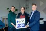 Three colleagues stand together in an office and hold a cube featuring the Ecologic Institute logo. The group smiles at the camera in a bright meeting space, symbolising leadership, collaboration, and teamwork within the organisation.