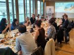 Participants seated around a conference table during a parliamentary breakfast discussion on local marine conservation. The meeting takes place in a bright conference room overlooking government buildings, with presentations by ADRA, Rare, and partner organisations displayed on a screen. Attendees engage in dialogue while sharing breakfast, highlighting stakeholder exchange on marine protection, conservation policy, and sustainable development