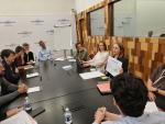 Participants sit around a conference table during a workshop at the Banque de France. A young woman presents findings using a printed visual aid while attendees listen and engage in discussion. The meeting focuses on knowledge exchange, stakeholder dialogue, and collaborative work in a professional setting.