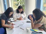 Three participants work together at a table, reviewing and annotating printed documents during a group session.